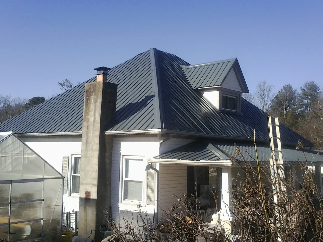 Dark blue standing seam metal roof on a white farmhouse with dormer — Slate & Tile Roof Repair by Roofing Brothers in Pine Prairie
