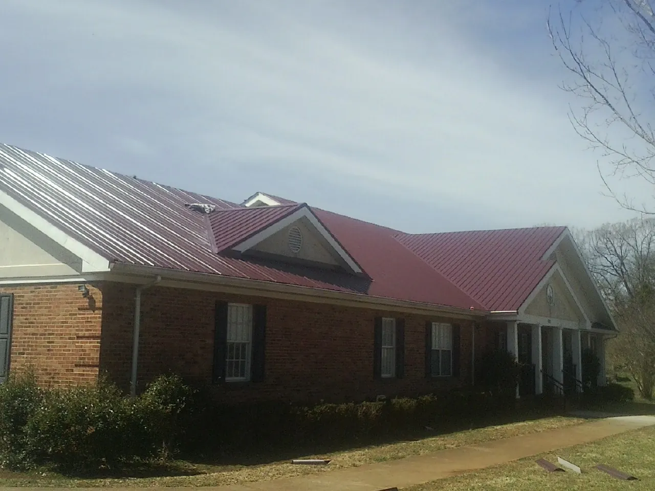 Red metal roof with gabled entries on a long brick building, from a Hail Damage Roof Repair job in Pine Prairie