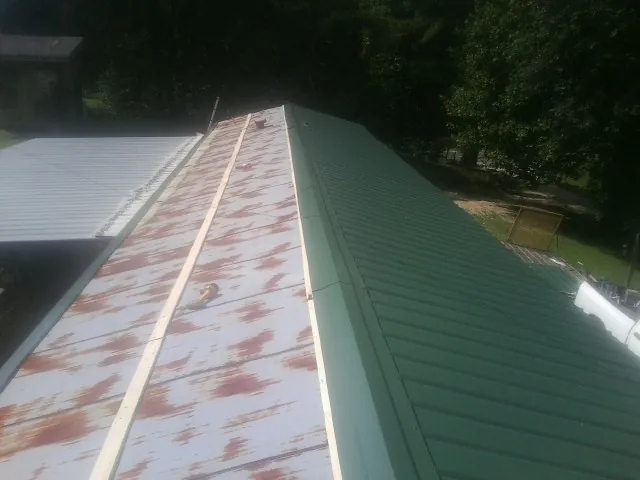 Old rusted panels beside newly installed green metal roofing — Wind Damage Roof Repair by Roofing Brothers in Pine Prairie