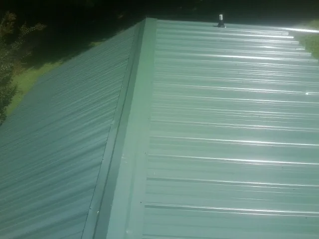 New green metal panels meeting at the ridge of a roof — Flat Roof Repair work by our crew in Pine Prairie