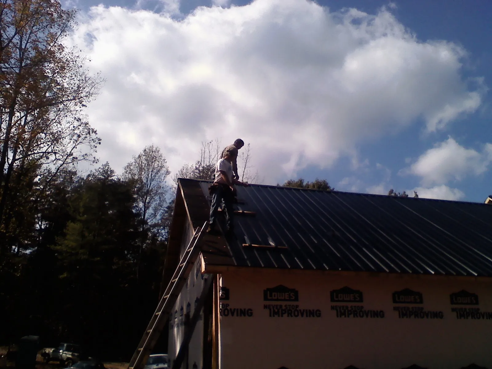 Roofer fastening dark metal panels high against a cloudy sky, from a Roof Inspection job in Pine Prairie