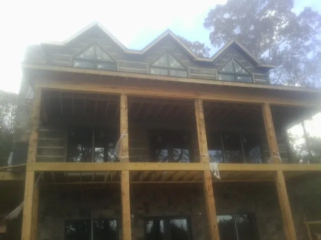 Dormers and porch framing on a large log home under construction — Roof Coating work by our crew in Pine Prairie