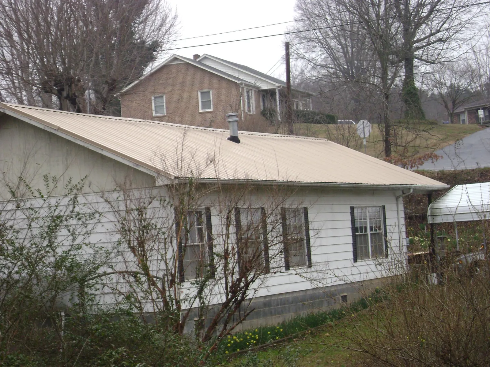 Tan metal roof on a white sided house set into a hillside — Commercial Roofing by Roofing Brothers in Pine Prairie