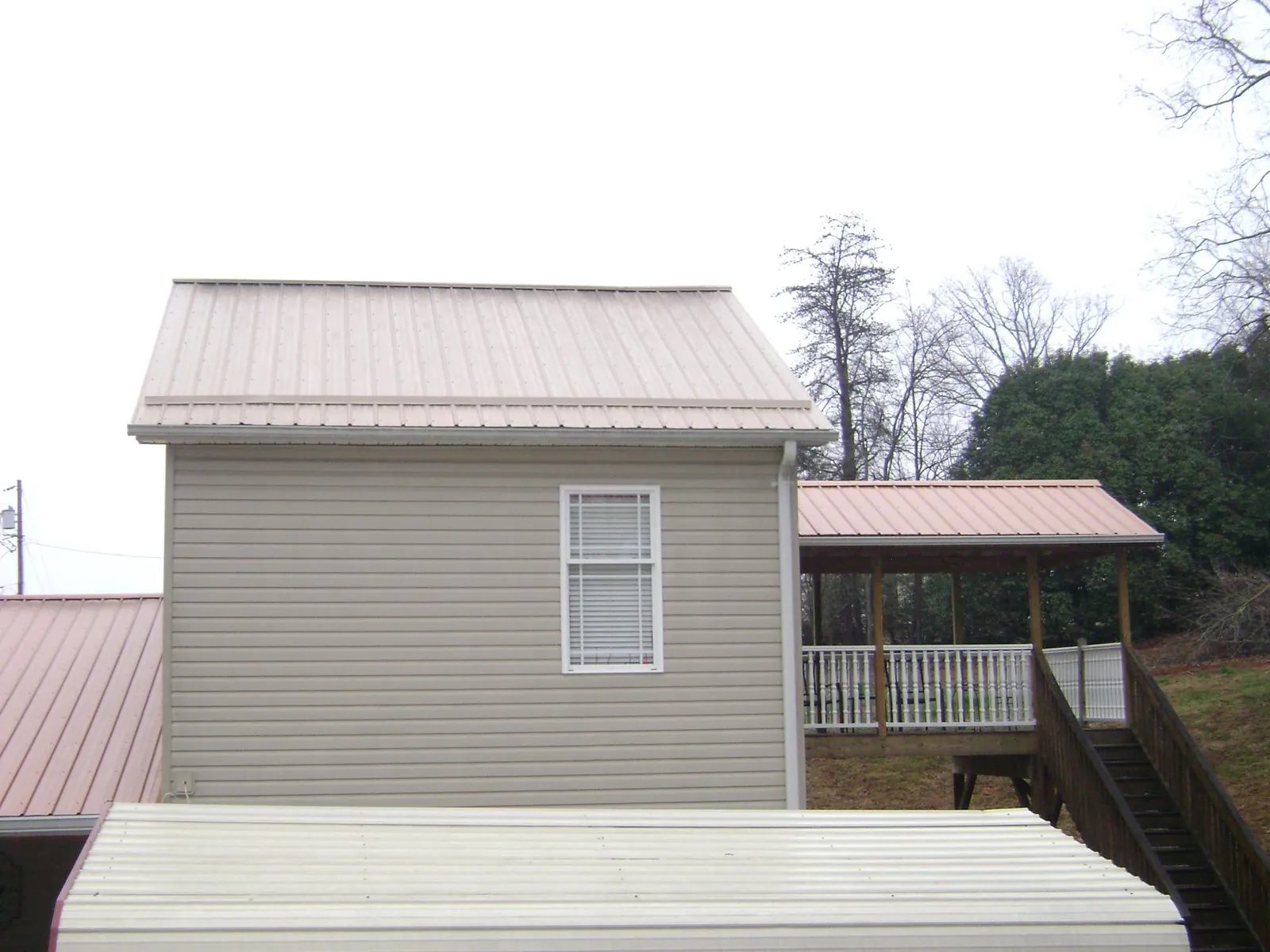 Tan metal roofs on a two story addition and attached porch, from a Roof Replacement job in Pine Prairie